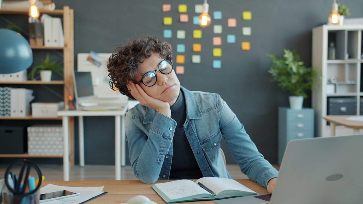 Person resting head on desk, visibly fatigued during work hours